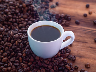 Set of coffee beans pilled on brown table and coffee cup full of aromatic espresso, close up view. Texture of wooden table. Selective soft focus. Blurred background