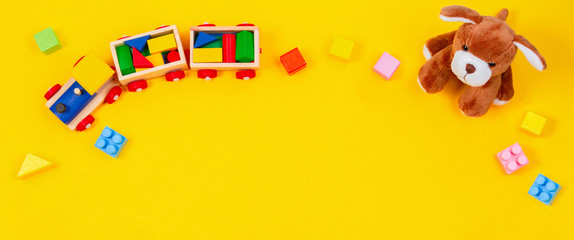 Kids toys background. White teddy bear, wooden train and colorful blocks on yellow background