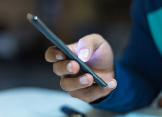 A man holding the hands of a mobile phone, is looking for online work on the Internet or social connection with the application for digital devices with 5G technology in an internal coffee shop.