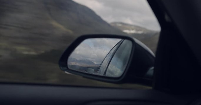 4K Travellers Car Side View Mirror within Glen Coe Scottish Mountains. Tourists Reflection of Hills, trees and Nature in Scenic Scotland.