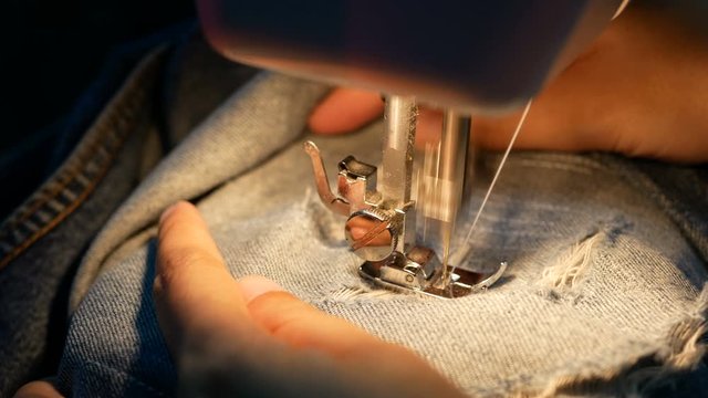 4K. close up of a woman sewing for repair blue denim jeans with a sewing machine