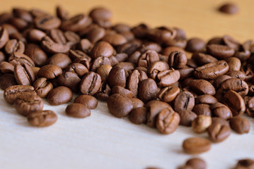 Roasted coffee beans scattered on a wooden surface close up