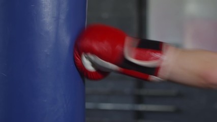 Side view of hands of unrecognizable female boxer in red gloves hitting heavy bag in gym - Powered by Adobe