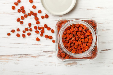 Obraz na płótnie Canvas Dried Rowan berries in a glass jar on a white table. Selective focus, top view, copy space