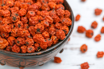Dried Rowan berries in a ceramic bowl on a white table close-up. Selective focus, copy space