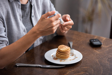 cropped view of woman with diabetes doing blood test with blood lacet near pancakes