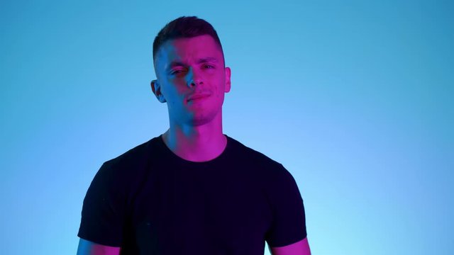 Vivid neon light and colors. A portrait of confident young guy. Man appraisingly contemptuously looks with arrogance at the camera
