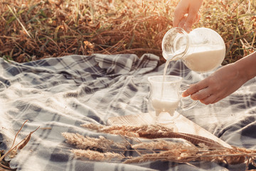 A woman pours milk from a decanter into a glass. Checkered plaid and wheat. Hands close up