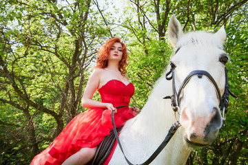 Girl in beautiful red dress on white horse in Park or forest. Photo shoot models and fashion