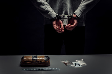 Arrested man in handcuffs with hands behind his back close-up on black background.