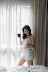 Fototapeta na wymiar Asian women while reading book near window with shear curtain / bedroom concept / copy space