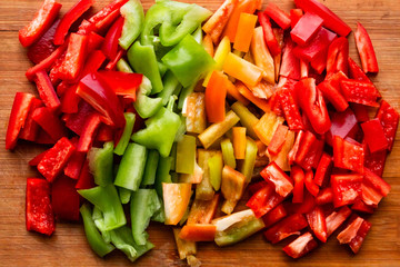 colorful chopped bell peppers - red, yellow, green - cut in big cubes on the wooden board
