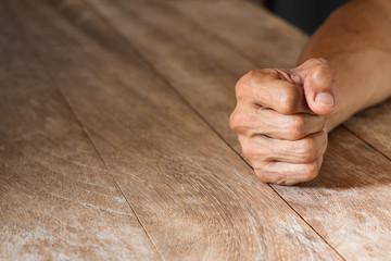 Man's clenched fist on vintage wooden table