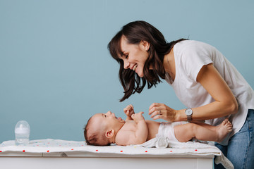Mother changing diaper on her baby on table over blue background. - obrazy, fototapety, plakaty