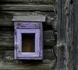 an old mailbox with cracked purple paint hangs on the wall of an old wooden house