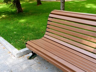 Photo of a brown bench in a park, with a stone-paved pathway and bright green grass in background. Wooden bench in a park.