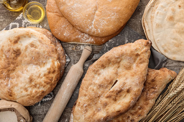 top view of lavash bread in diverse shapes near rolling pin and olive oil on wooden table