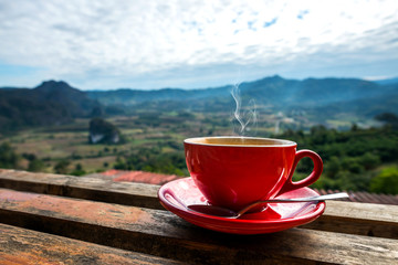 A cup of coffee with smoke on wood table, blurred estate scenic background, high angle view. Morning coffee cup
