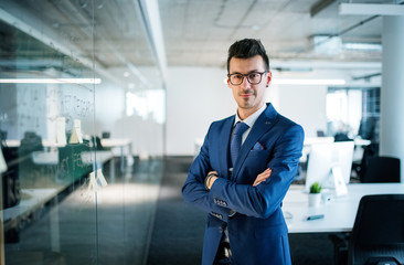 A portrait of young businessman standing in an office, arms crossed.