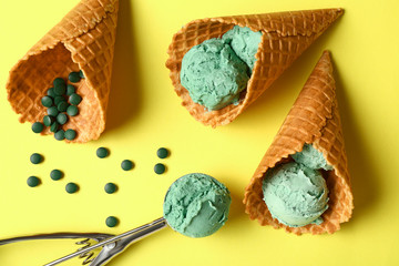 Waffle cones with tasty spirulina ice-cream on color background