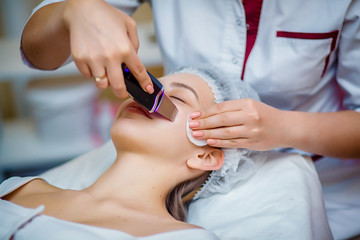 Woman receiving ultrasonic facial exfoliation at cosmetology salon. Procedure clearing clogged...