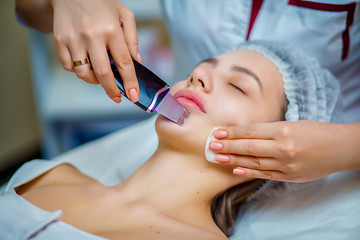Obraz na płótnie Canvas Woman receiving ultrasonic facial exfoliation at cosmetology salon. Procedure clearing clogged pores, ultrasonic treatment for skin rejuvenation, beautician uses modern apparatus for refreshing