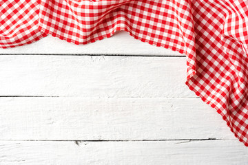 Red checkered tablecloth on white wooden table. Top view