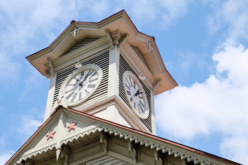 Fototapeta na wymiar Sapporo, Japan July 20, 2016: Sapporo Historic clock tower famous sightseeing spot on blue clouds sky background in summer time, the clock construct at the top of retro roof in Hokkaido.