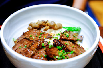 Beef grilled rice bowl, paprika and leek  on top with cap of mushroom boiled and vegetables in white bowl put on the tray. Japanese food traditional Gyudon beef in restaurant.