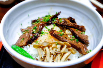 Beef grilled rice bowl, paprika and leek  on top with cap of mushroom boiled and vegetables in white bowl put on the tray. Japanese food traditional Gyudon beef in restaurant.