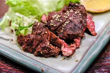 Being Grilled ribeye beef steak medium rare sliced on top of seasoning sesame,beef and vegetables serve on ceramic plate put on the wooden table.