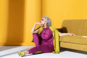 Curly woman in pink suit sitting on the floor near sofa
