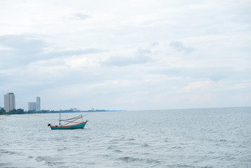 Obraz premium Small Thai fishing green boat in the sea water waving on city and building background.Commercial fishing boat on the sea ,small fishing trawler flooding on the water with blue clouds sky in Thailand.