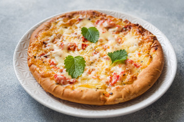 Homemade pizza tortilla with tomato and cheese on gray concrete background.