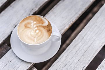 White big cup of coffee with art on white wooden table with copy space.