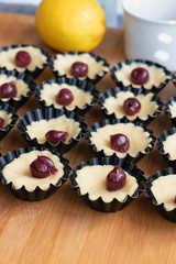 Small tarts with cherry and whipped egg whites and pistachio filling in metal forms before baking showing the process