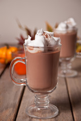 Two glass of hot creamy cocoa with froth with autumn leaves and pumpkins on the background