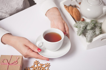 Woman's hand holding cup of tea. Christmas decor on the background.