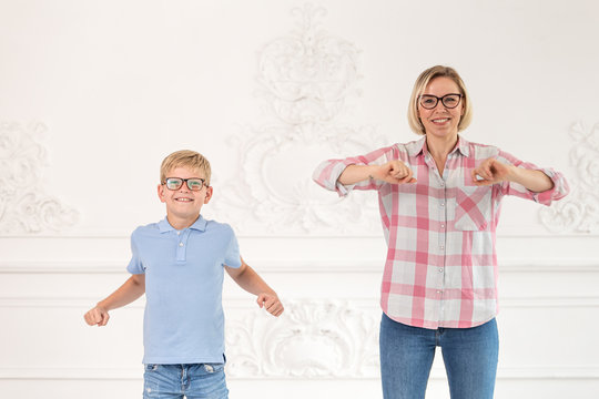 A beautifull mother in a plaid shirt and her little son in a blue shirt do exercises and warm up. Boy waving his hands to the sides, while his mother bending her hands in front of her