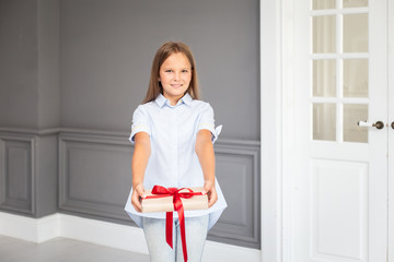 A young girl in light blue shirt holds out a gift to the camera. Selective focus