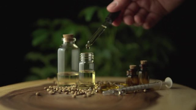 Close look to pharmacist or scientist working with pharmaceutical medical cbd oil. Various medicine options on the on wood table, such as pills and oils in the jars for oral use. Cannabis hemp plant.