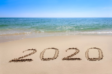 Year 2020 written at the sand beach with sea wave water
