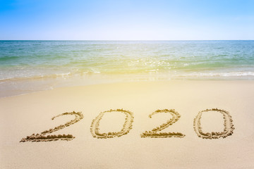 Year 2020 written at the sand beach with sea wave water