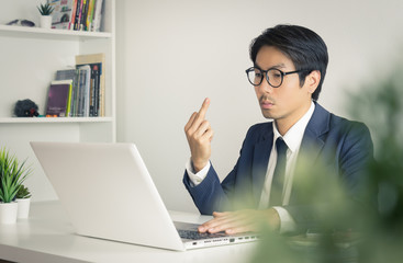 Angry or Irritable Asian Businessman in Formal Suit Show Middle Finger in front of Laptop Screen in Vintage Tone