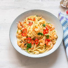 Shrimp noodles in garlic sauce with herbs and hot chili peppers in a rustic bowl, top view