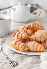 Homemade roll-shaped shortbread. Sprinkled with sugar. On a white plate. Background gray linen. In the background is a white teapot and a cup. Country style.