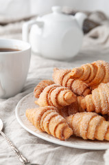 Homemade roll-shaped shortbread. Sprinkled with sugar. On a white plate. Background gray linen. In the background is a white teapot and a cup. Country style.