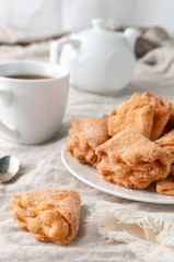 Homemade triangle cookies with curd filling sprinkled with sugar. On a white plate. Background gray linen. In the background is a former teapot and cup.