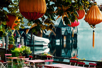 Chinese lanterns on a chestnut tree against the backdrop of an Alpine lake and boat sheds in the early summer morning