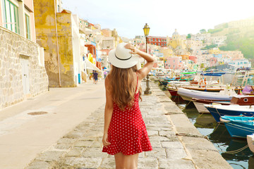 Holidays in Italy. Back view of beautiful girl in stunning colorful harbor of Procida, Italian Capital of Culture 2022.
